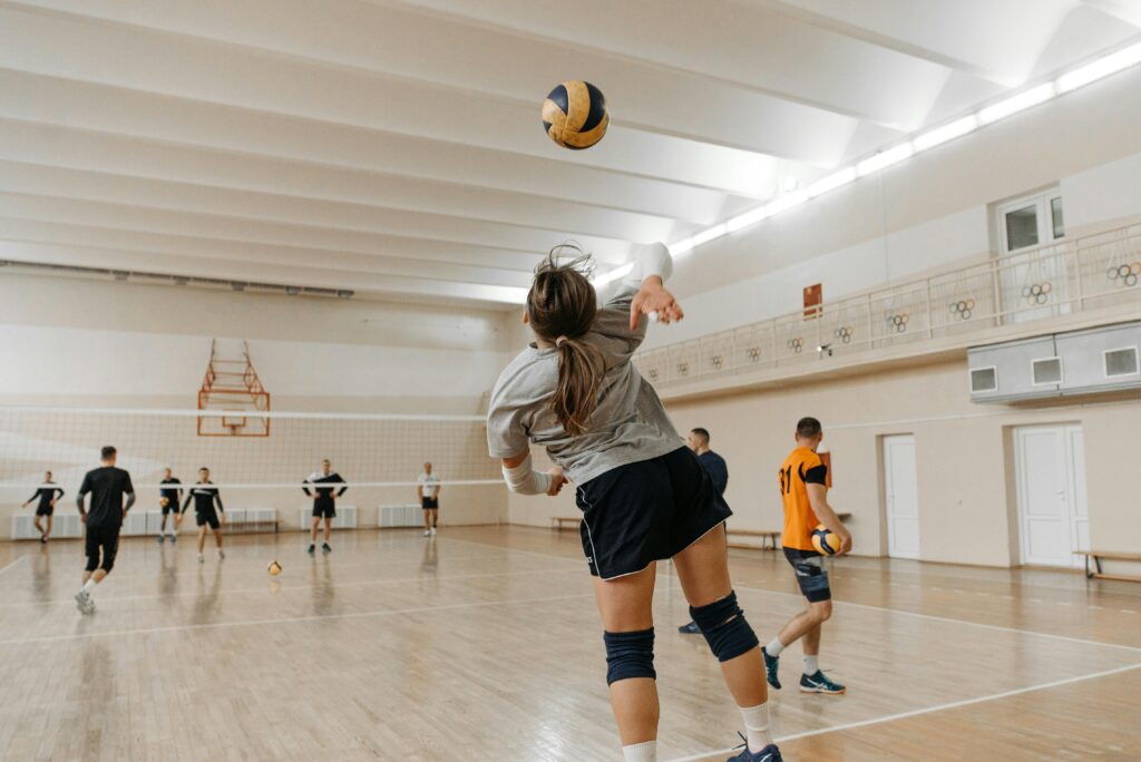 Team practicing volleyball indoors, focusing on a player's serve with active participants.